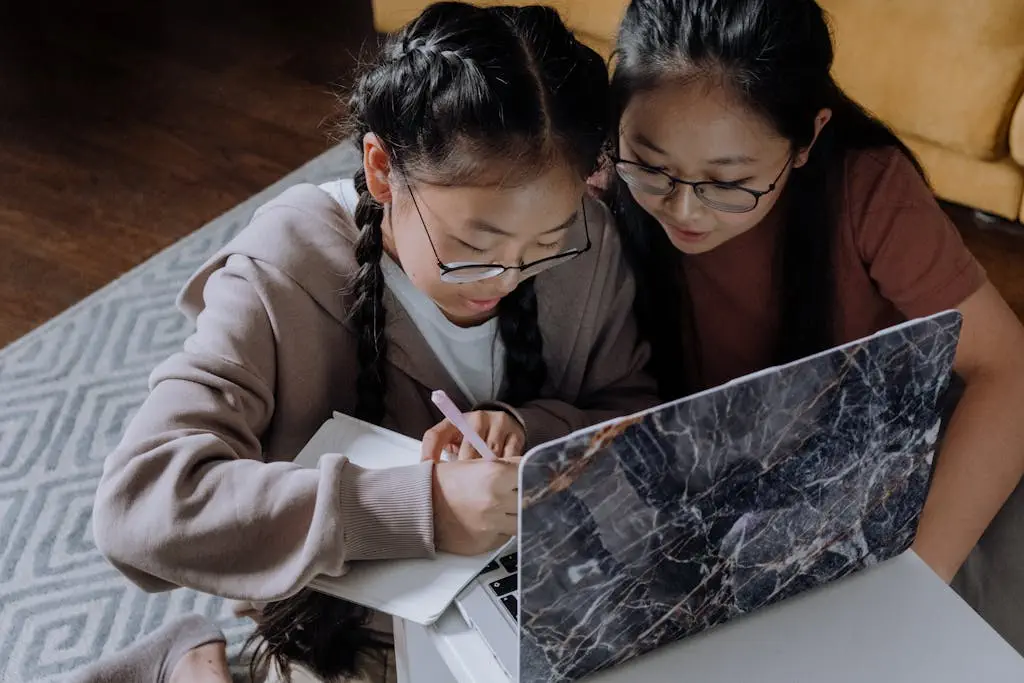 Two sisters studying together at home, using a laptop and writing in a notebook, fostering learning and family bonding.